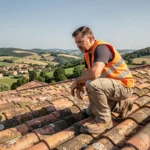 Couvreur professionnel travaillant sur un toit en tuiles traditionnelles dans la Drôme avec vue sur les collines provençales